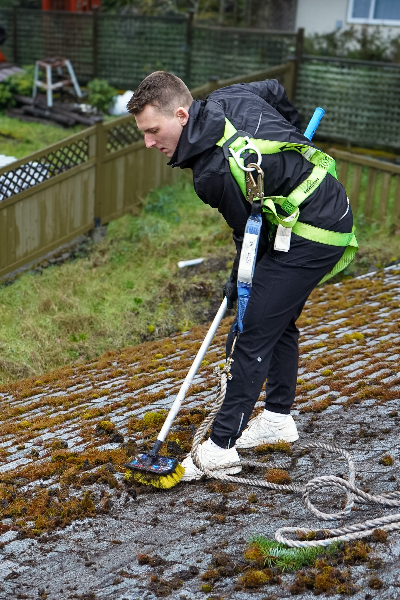 Craig brushing moss from a roof while wearing a harness